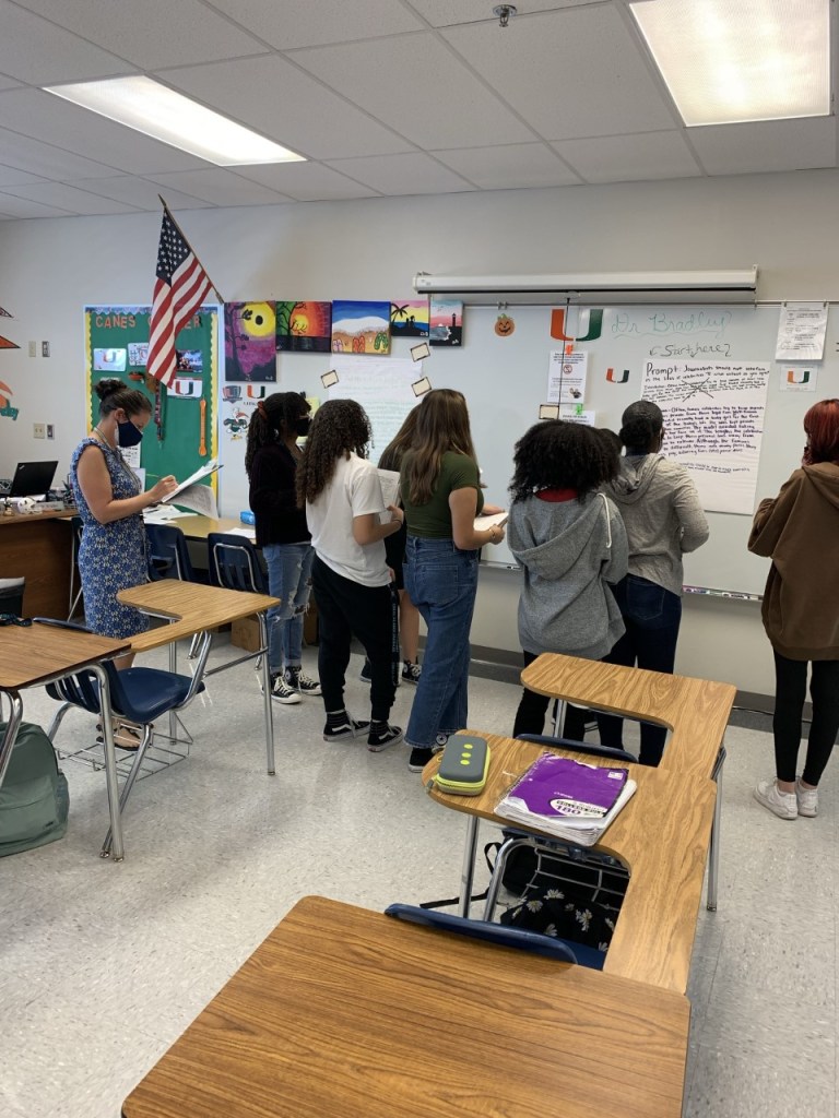 students reading essays posted on classroom wall